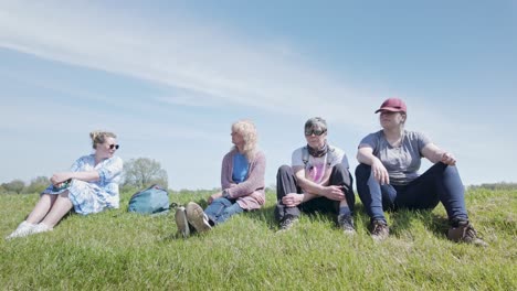 Four-relaxed-mixed-age-women-sitting-on-grass-bank-enjoying-views-with-dog