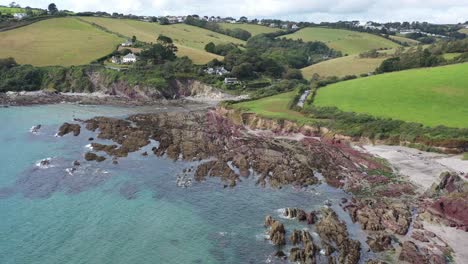 Wide-push-out-reveal-shot-of-Talland-Bay-on-the-Cornish-coast,-revealing-surrounding-countryside-landscape