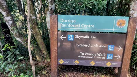 camera slowly pans across a trail sign at dorrigo rainforest centre, surrounded by dense foliage in natural daylight, highlighting walking directions and distances