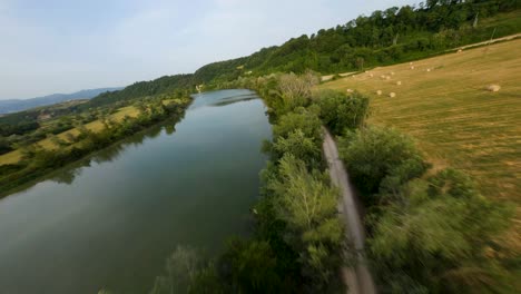 flying over a large river near a hay bales field with an fpv drone at sunset