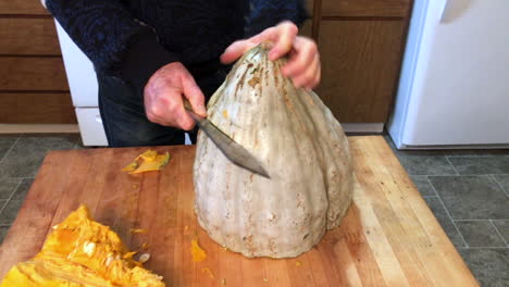 Man-in-home-kitchen-cutting-a-large-pumpkin,-called-Blue-Hubbard-Squash,-and-struggling-with-the-size-of-the-vegetable