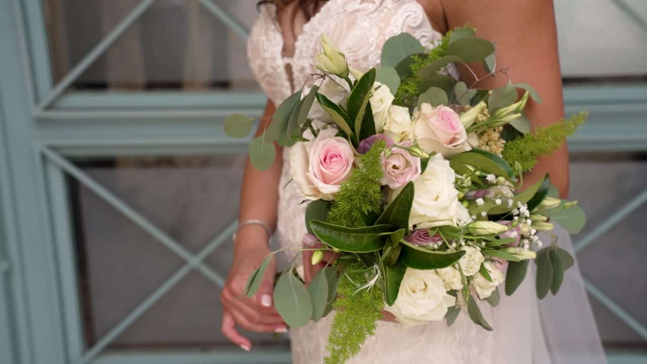 Una sposa è in piedi con grazia, mostrando il suo splendido bouquet da sposa pieno di rose delicate e verdeggiante. L'ambiente elegante fa da cornice al suo momento di gioia