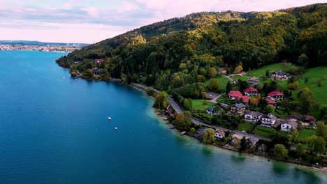 Tranquil-village-nestled-on-a-lake-shore,-vibrant-autumn-foliage-paints-the-surrounding-mountains