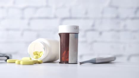 hand holding a medicine bottle with spilled pills and a thermometer nearby