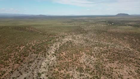 Ascending-drone-shot-of-a-dry-game-farm-with-mountains-on-the-horizon-during-drought-near-Okahandja,-Namibia