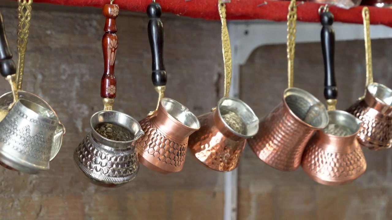 Turkey, Mardin, Traditional Turkish Coffee Pots in copper and in silver colors hanging on a rack, one copper pot is swinging joyfully.