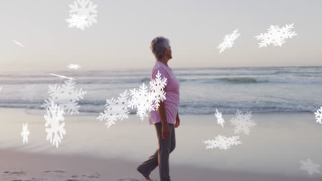 Animation-of-christmas-snow-falling-over-biracial-woman-on-beach