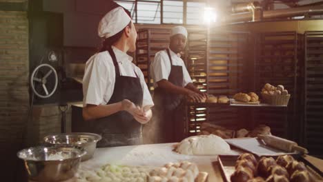 Animation-of-happy-asian-female-baker-cleaning-hands-from-flour-and-talking-with-male-coworker