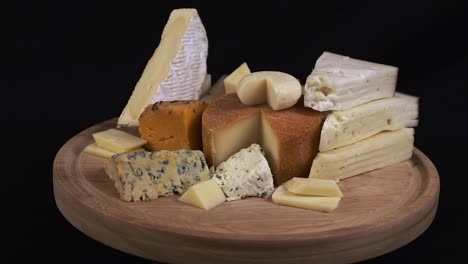 Assorted-cheese-platter-on-wooden-board-rotate-on-black-background