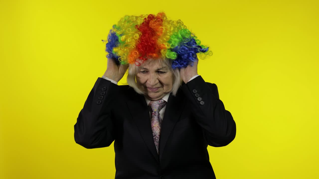 비즈니스 슈트를 입은 고위 여성이 조롱거리 가발을 입고 일하기 시작하고 미소 짓습니다.