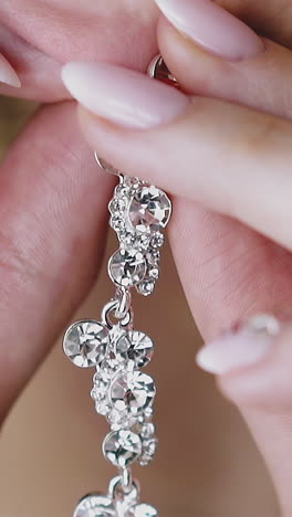 cu, slow motion: young elegant woman with gentle manicure puts on beautiful long silver earring decorated with numerous shiny gems close view