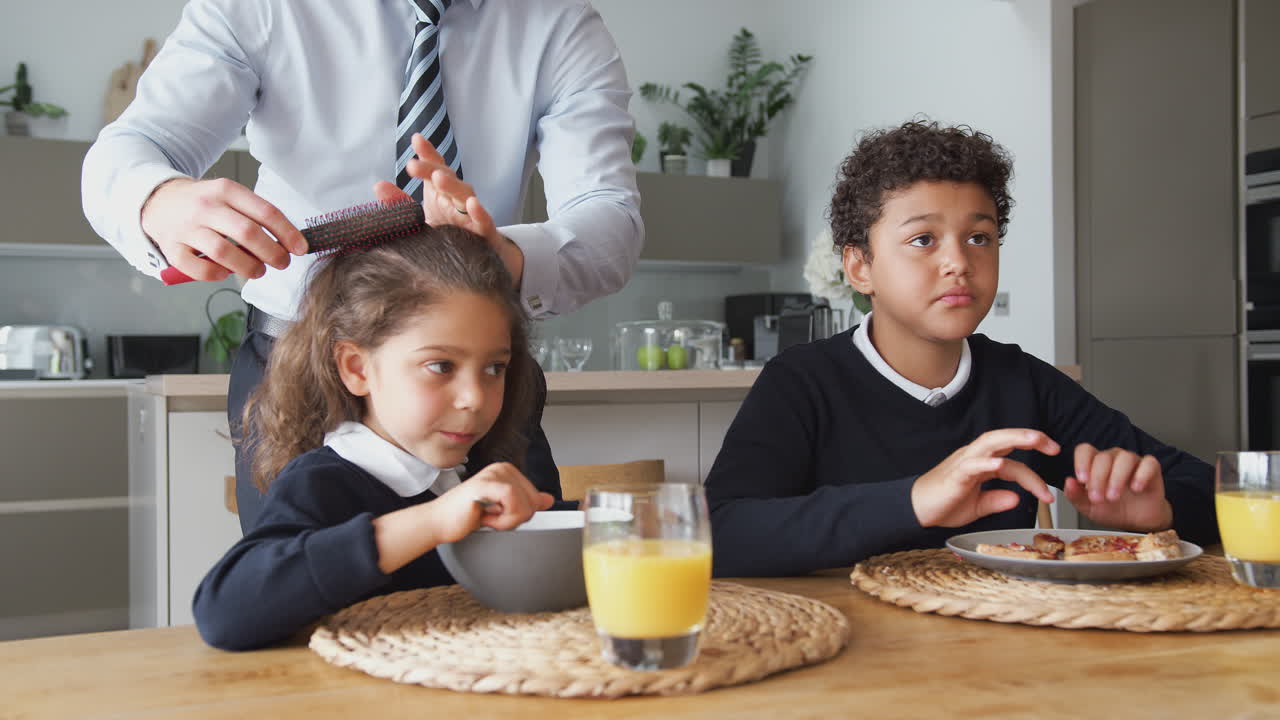 padre empresario en la cocina cepillando el cabello y ayudando a los niños con el desayuno antes de la escuela