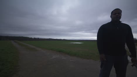 modern black swordsman warrior awaiting battle opponent in open field under grey sky, europe, 4k | muscular, intimidating, shadow, figure, blurry, dark clothes, powerful, close up, stance adjust