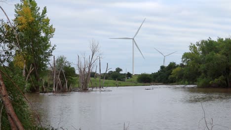 un estanque de granjeros inundado rodeado de árboles con turbinas eólicas en la distancia en un día nublado en nebraska, ee.uu.