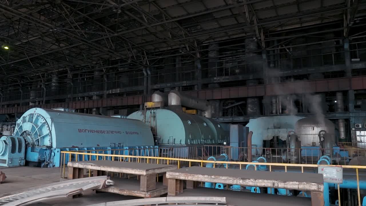 Blue large turbines for electricity production in the middle of the hall at a coal-fired power plant. Pipes with smoke. Outdated polluting energy production technology
