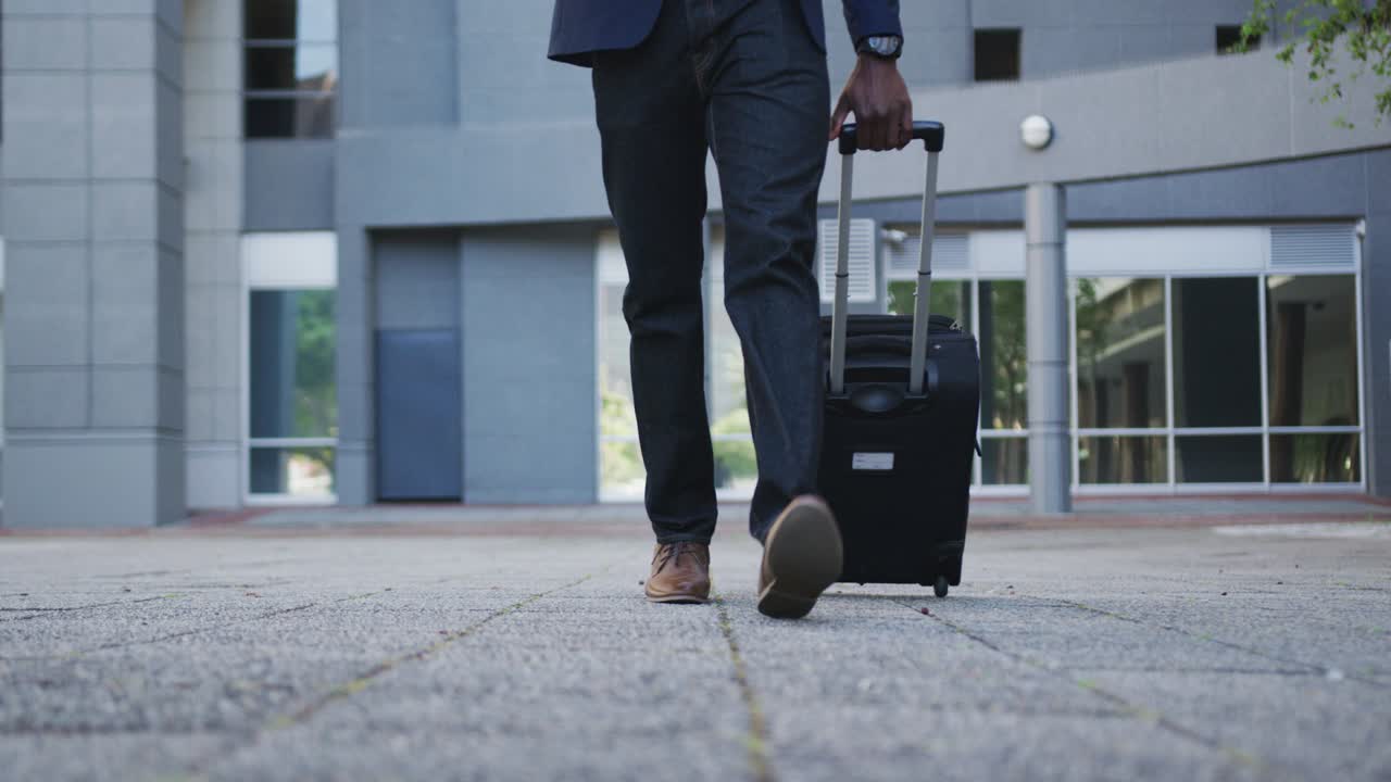 bassa sezione di uomo d'affari afroamericano che cammina con una valigia in strada