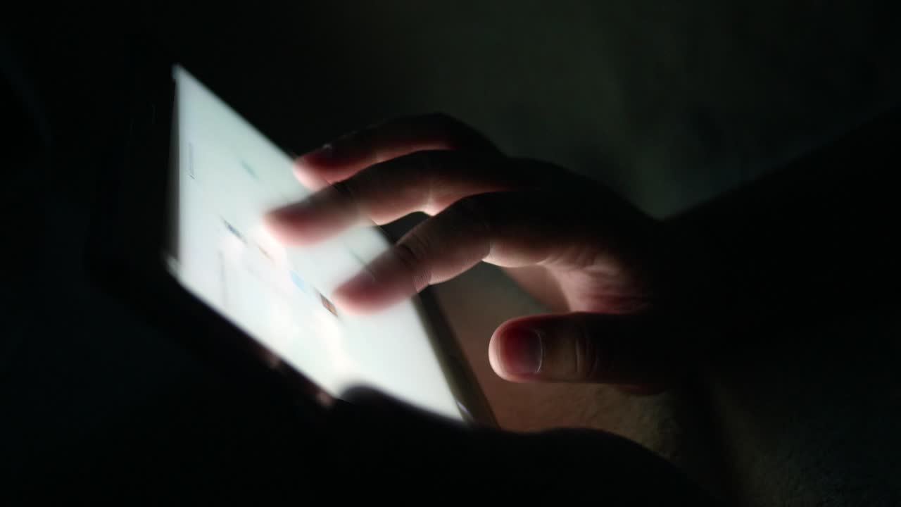Giovane uomo con tablet touch screen in mano scorre lo schermo mentre cerca immagini o legge notizie online in una stanza di notte