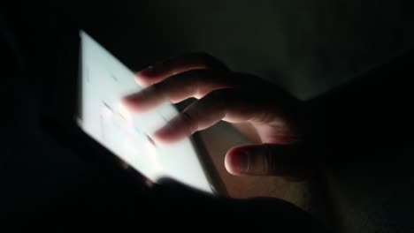 young man holding tablet touch screen the device in his hands and he is scrolling the screen while searching for pictures or reading news feed online at night room