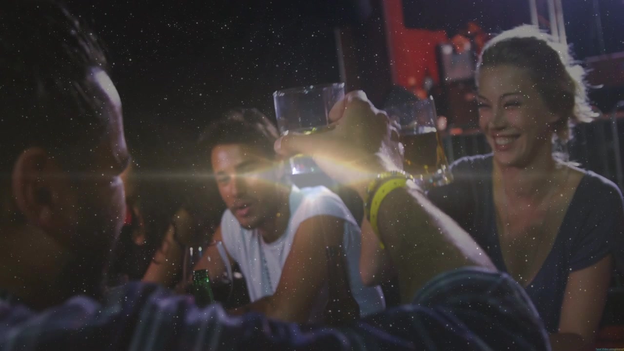 Front man raising glass, leading woman mirroring mug, group toasting under lens flare, hospitality