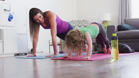 caucasian mother and daughter practising yoga in living room