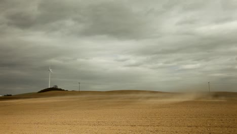 White-three-bladed-wind-turbine-in-a-barren-light-brown-field-under-a-grayish-cloudy-sky,-exuding-a-desolate-and-lonely-aura