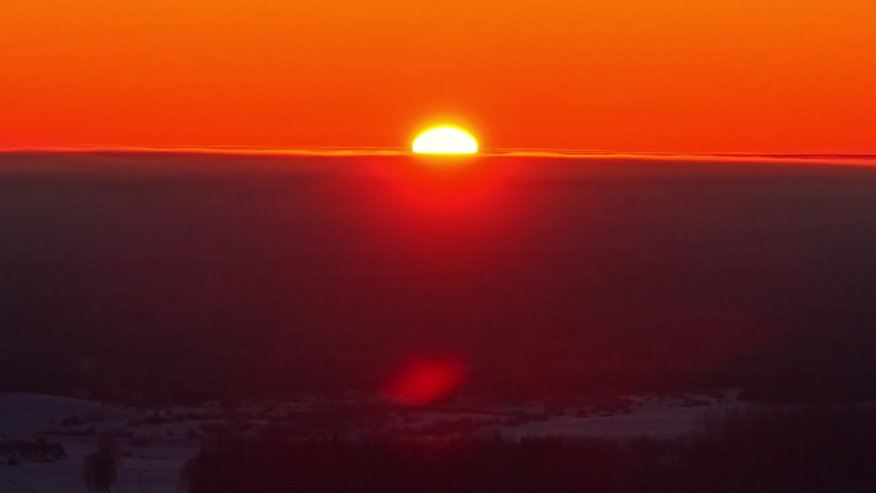 Auringonlaskun timelapse, jossa suuri aurinko hehkuu pilvien yllä horisontissa luoden dramaattiset taivasolosuhteet, ilmakuva.