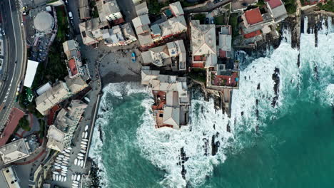 Top-down-aerial-view-of-waves-crashing-into-Genoa-coastline-lined-with-buildings