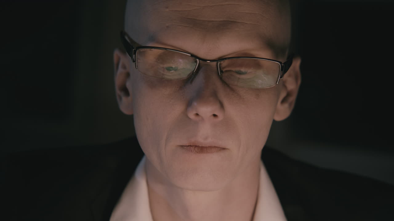 Pale bald accountant looks through the tax papers in the weird room at night