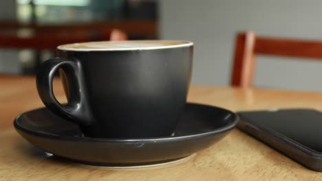 a black cup of coffee and a smartphone on a wooden table