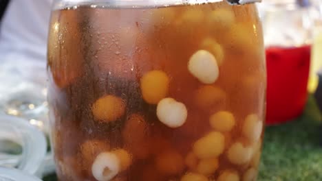 vendedor de alimentos agitando jugo de longan con carne fresca de longan en un gran frasco de vidrio en el puesto de jugo de fruta en la calle caminando