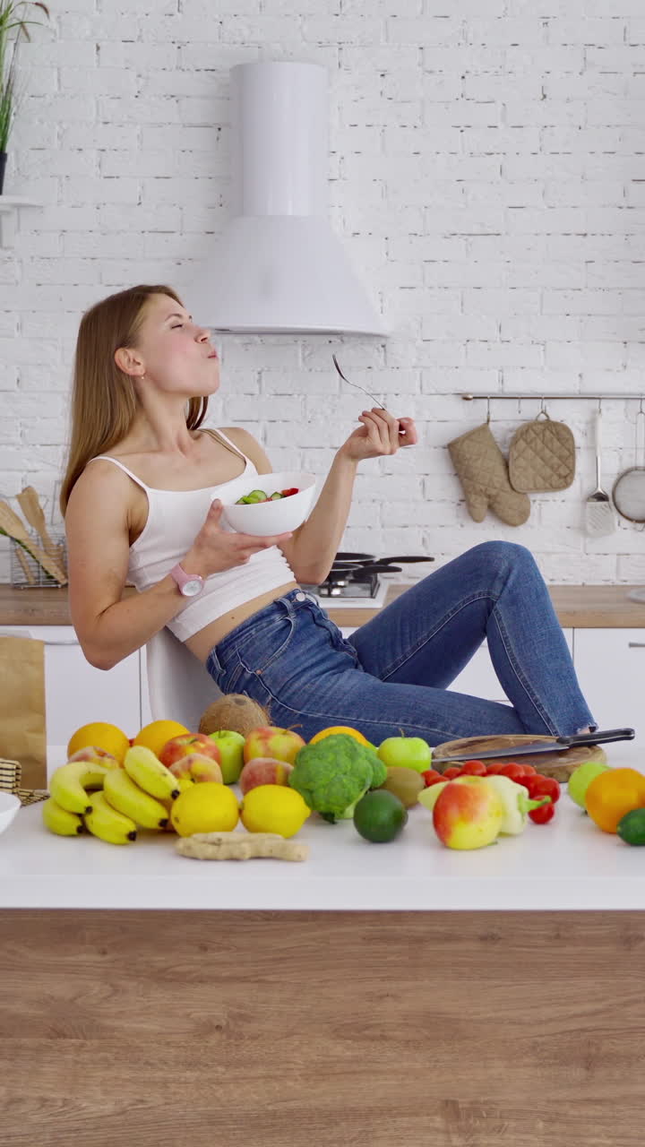 Happy woman eating vegan food. Modern kitchen background with fresh organic food on the table at home. Healthy lifestyle. Vertical video