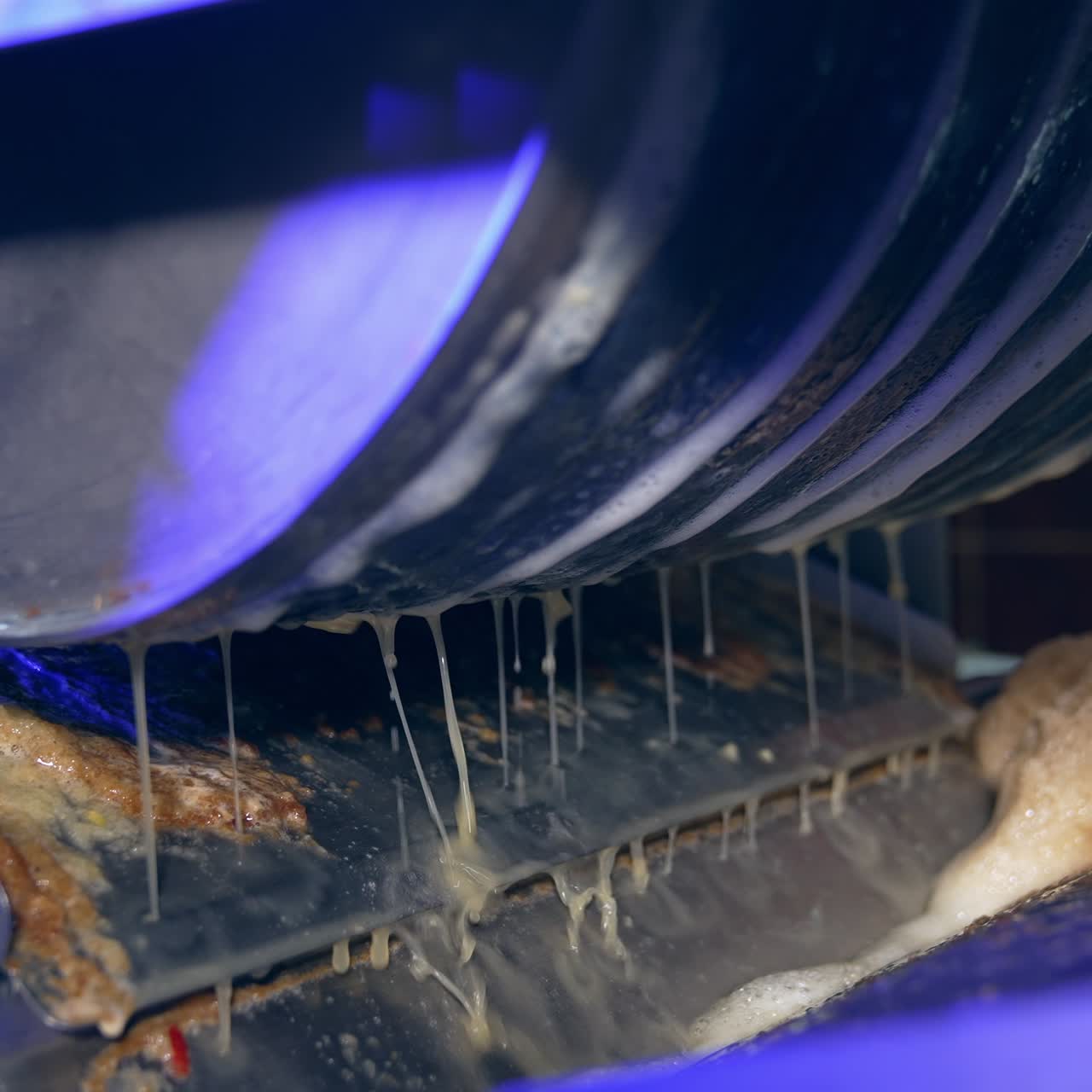Apple juice dripping from the rotating shaft. Machine squeezing fruit at automated line of food factory. Close up