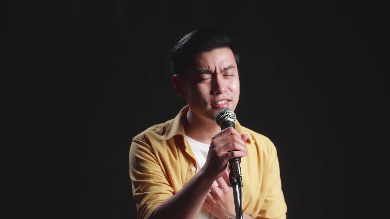 Asian Man Singer Singing Into Microphone On Black Background