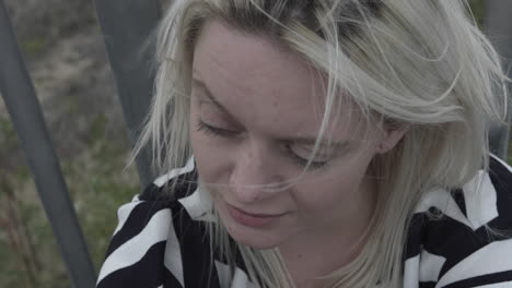 a young depressed woman sits curled up leaning against a fence