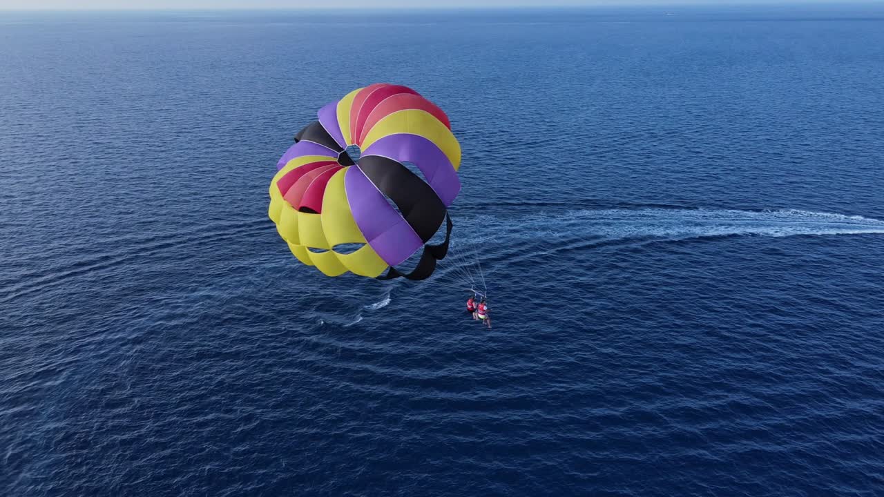 Couple Parasailing over Blue Ocean on Colorful Double Canopy Tugged by Boat, Drone View