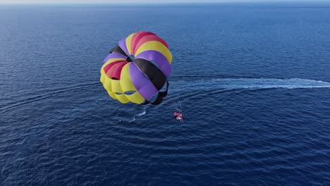 couple parasailing over blue ocean on colorful double canopy tugged by boat, drone view