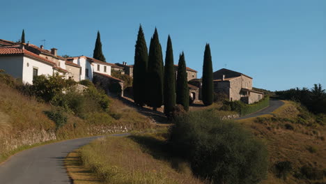 a picturesque village nestled on a hillside with a winding road and tall cypress trees under a clear blue sky