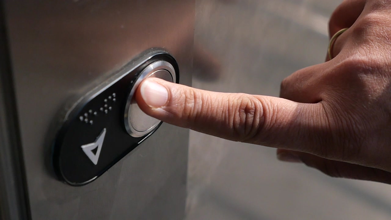 Close-Up of a Finger Pressing an Elevator Up Button with Braille