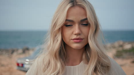 portrait luxurious blonde girl looking camera confident. woman posing sea shore.