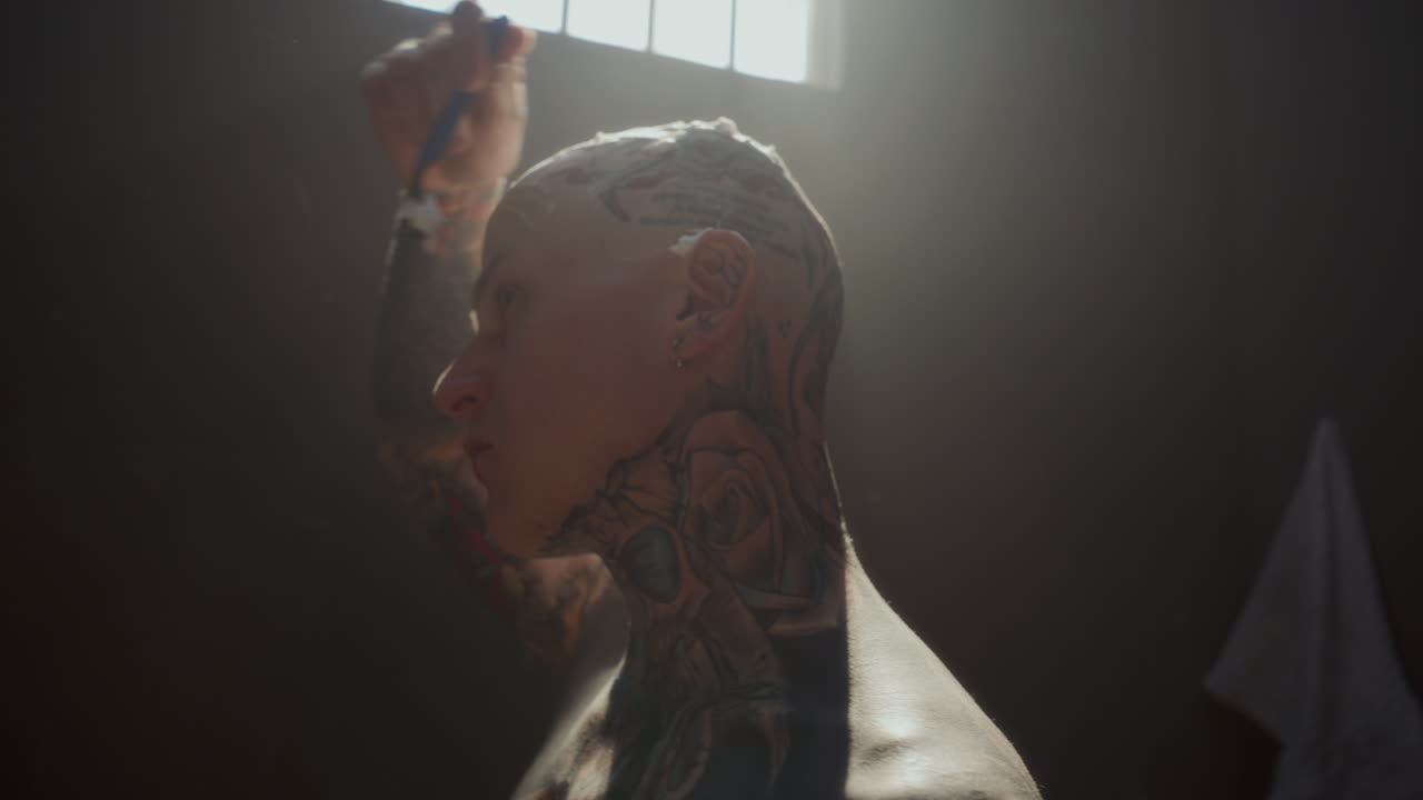 Tattooed Inmate with Foam on Scalp Shaving Head in Prison Cell