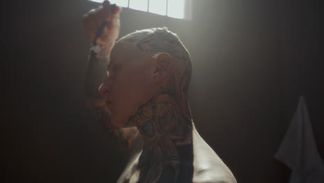 tattooed inmate with foam on scalp shaving head in prison cell