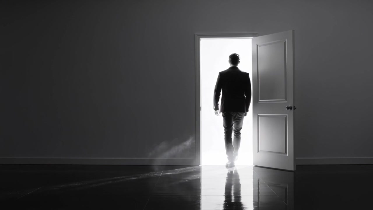 Uomo in abito che cammina verso un forte controluce all'uscita, con nebbia e pavimento lucido.