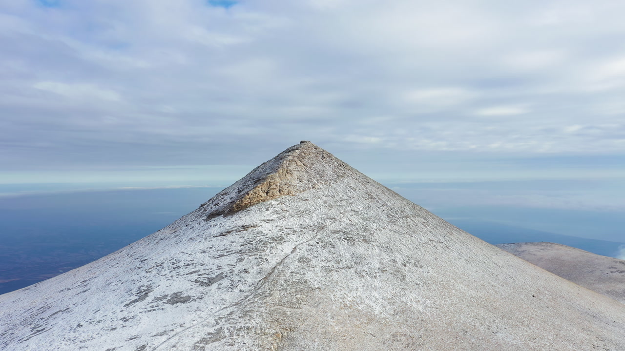 Aerial View of a Snow-Dusted Mountain Peak Under a Cloudy Sky