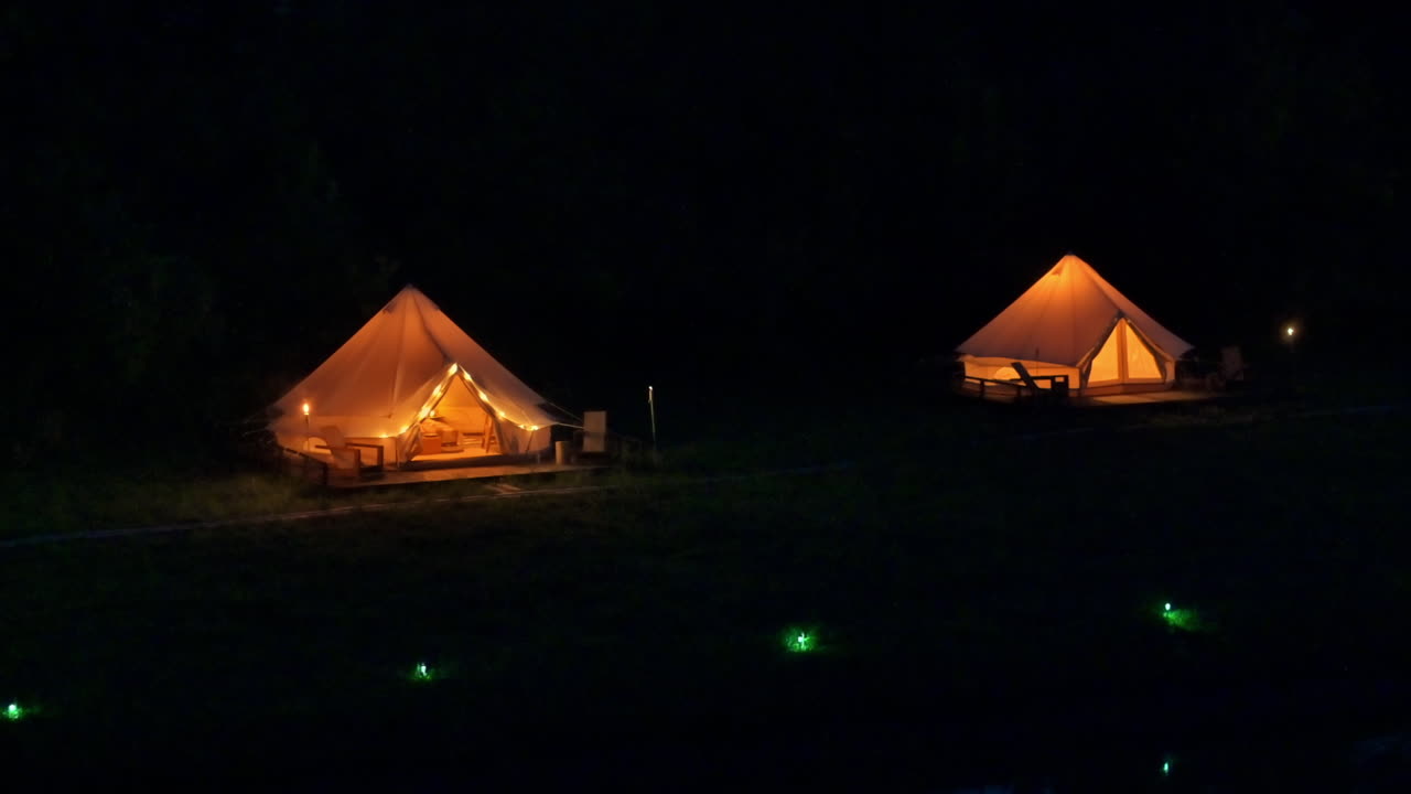 Telte med brændende fakler, lamper og træstole ved glamping om natten