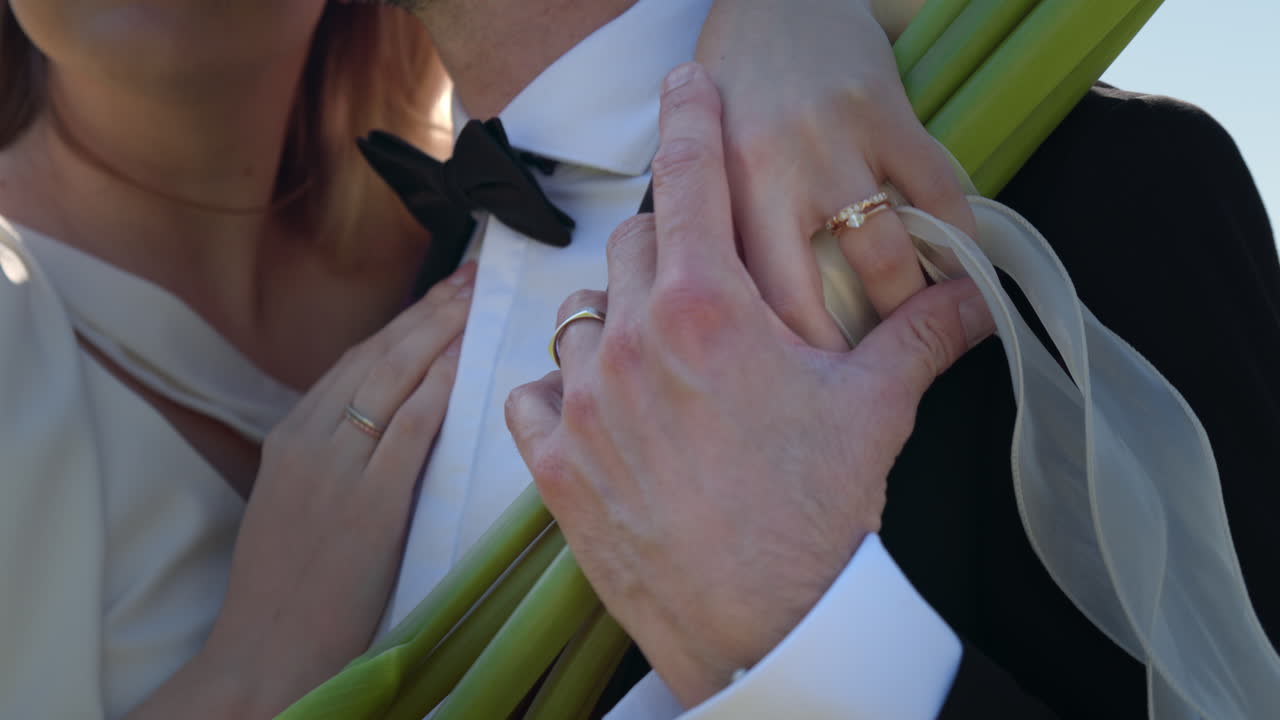 Bride And Groom Holding Hands With Rings On Bouquet Flower Stems. Close-up Shot
