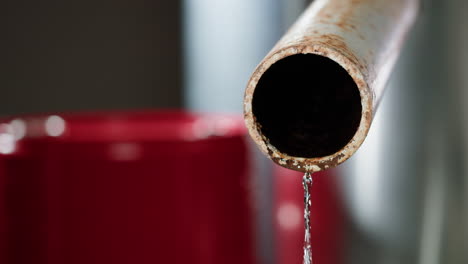 rusty pipe dripping water into red bucket