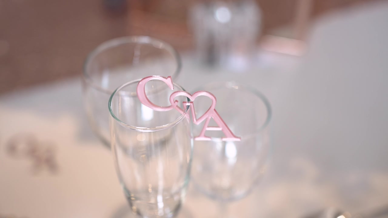 To glas er placeret på et bord med et dekorativt element, der viser et pars initialer. Rammen ser festlig ud og er sandsynligvis en del af en fejring.