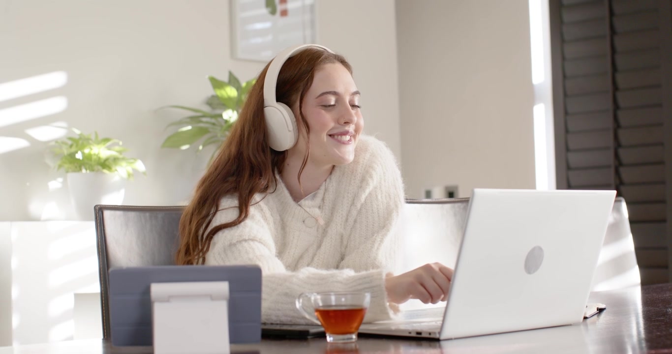 En kvinde i 20'erne, der får et opkald til et møde, bærer headset og læner sig mod en tablet ved bordet.