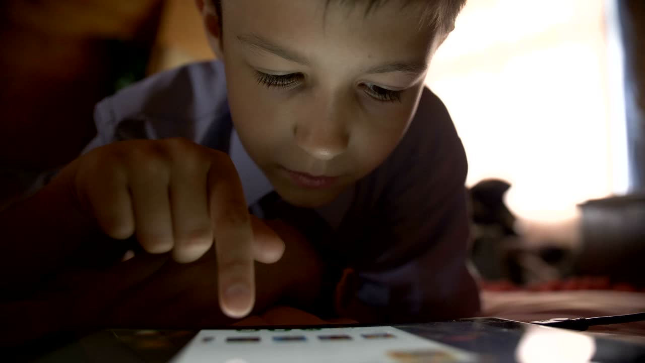 소년은 침대에 누워서 집에서 태블릿 pc를 만져요.