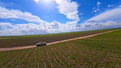ride of a futuristic tesla cybertruck by the farmlands. fpv drone footage of a modern auto with a blue sky at backdrop.